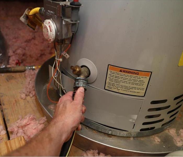 Hand attaches hose to a home water heater to perform maintenance in Philadelphia, PA.
