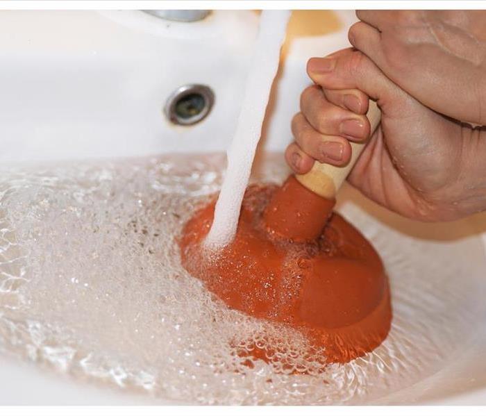 Woman with plunger trying to remove clogged sinks.
