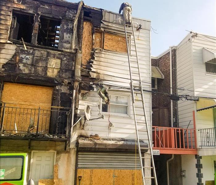 SERVPRO technician on a ladder in front of a Philadelphia home that recently experienced a fire